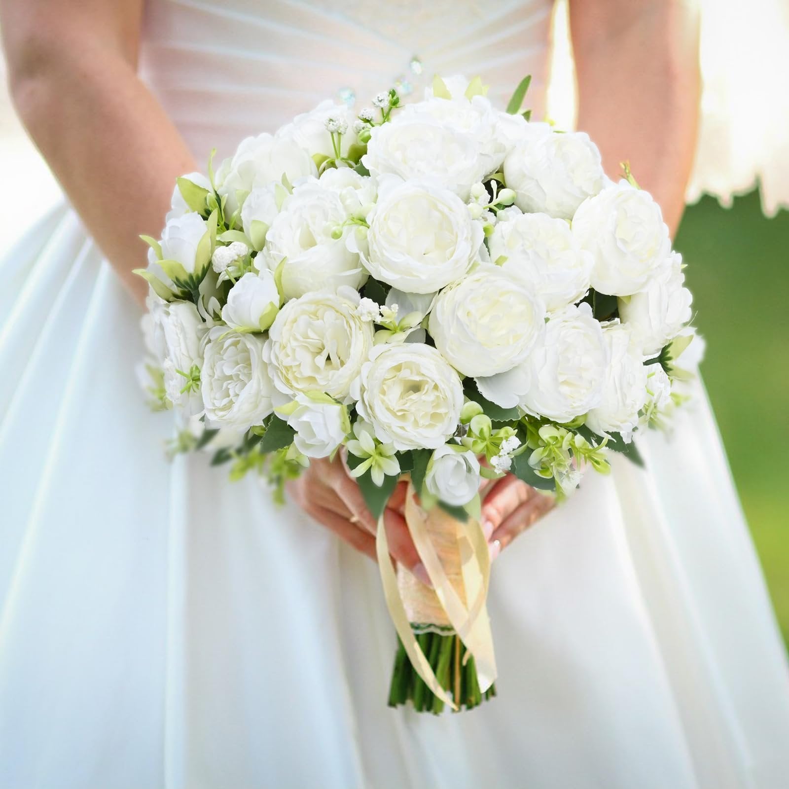 Bride holding a white artificial peony bouquet with satin ribbons and lace trim, wearing a white wedding dress.