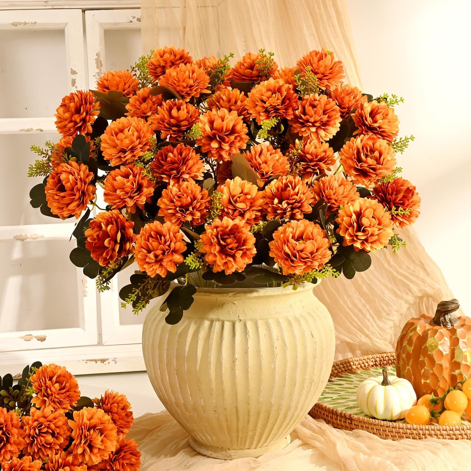 Arrangement of orange artificial mums in a textured vase, with decorative pumpkins and berries on a tray in the background.