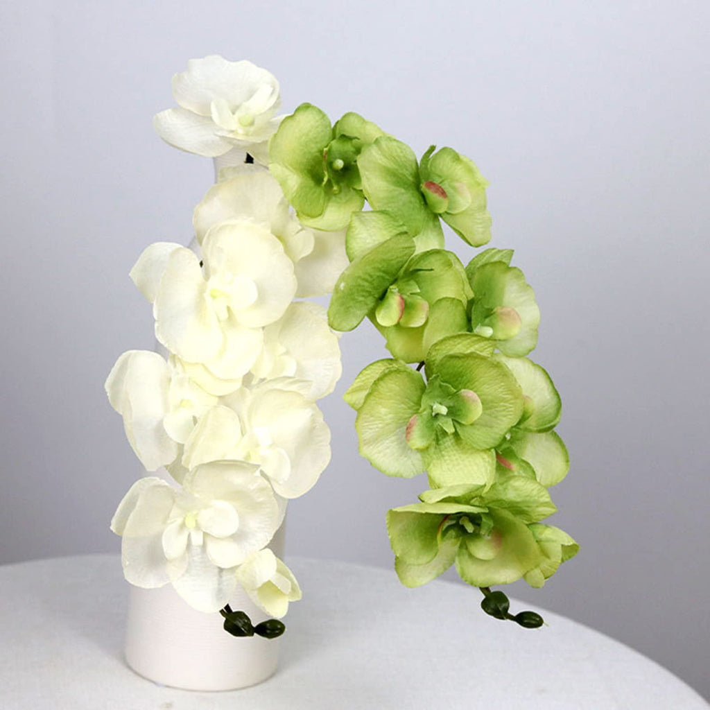 Two stems of artificial phalaenopsis orchids, one white and one green, in a white vase on a table.