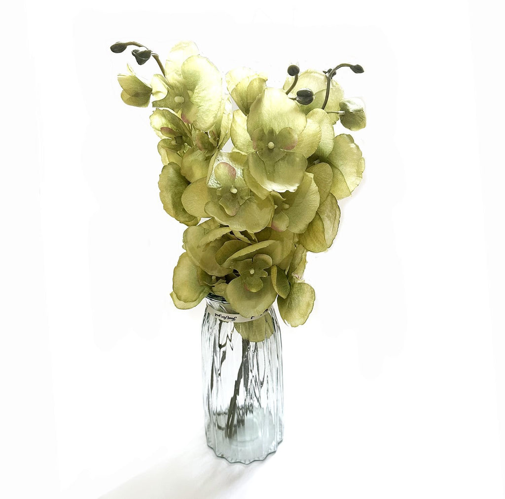 Green artificial phalaenopsis orchid stems in a clear glass vase with a decorative ribbon.