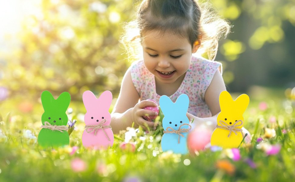 Four pastel wooden bunny decorations with twine bows in grass with a child playing