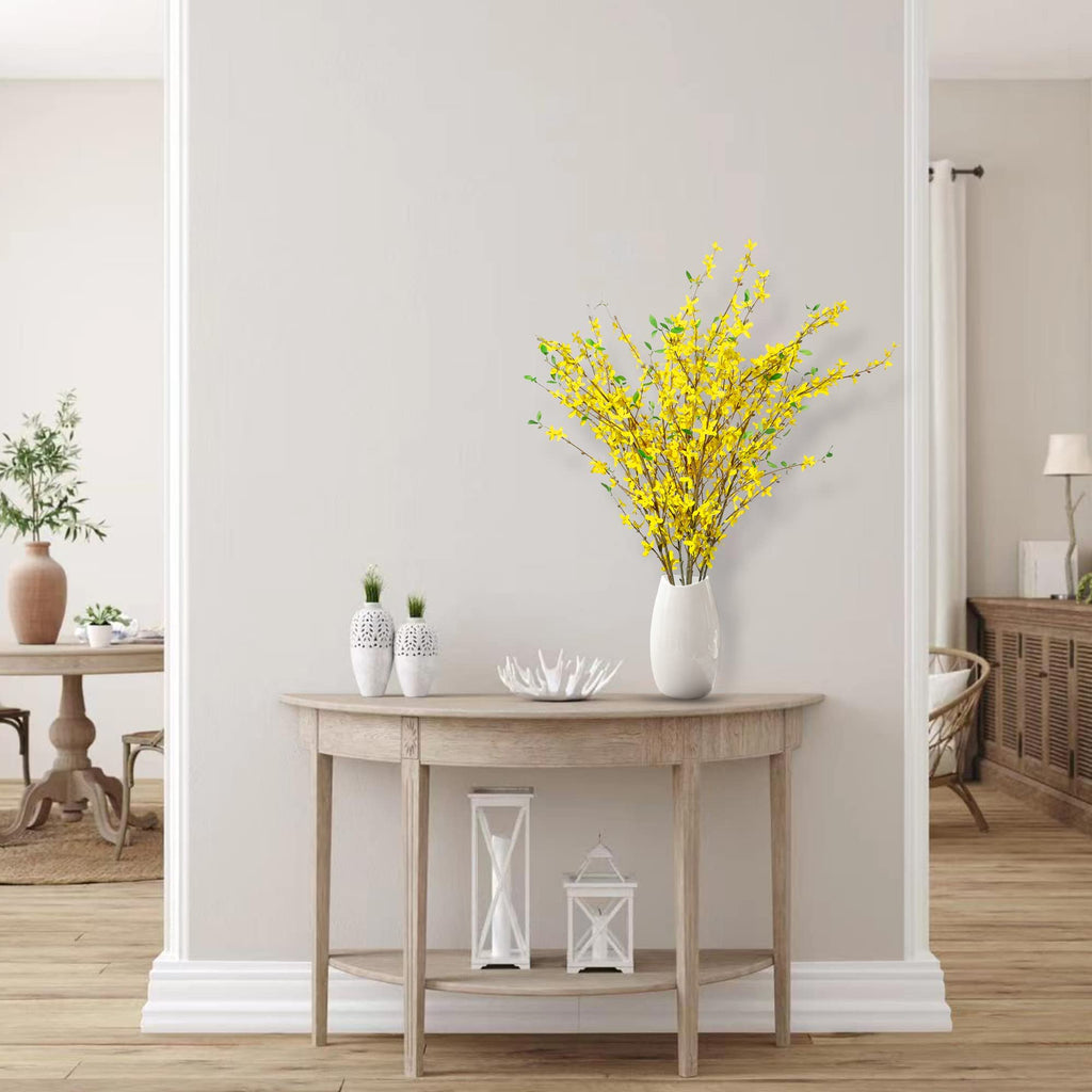 A vase of yellow forsythia branches on a console table in a hallway setting.