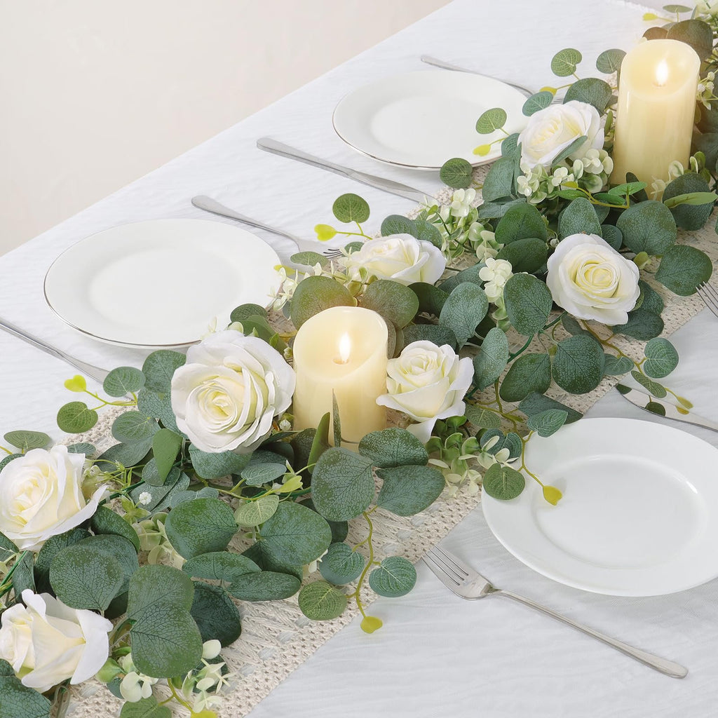 Artificial eucalyptus and white rose garland with candles on a table setting