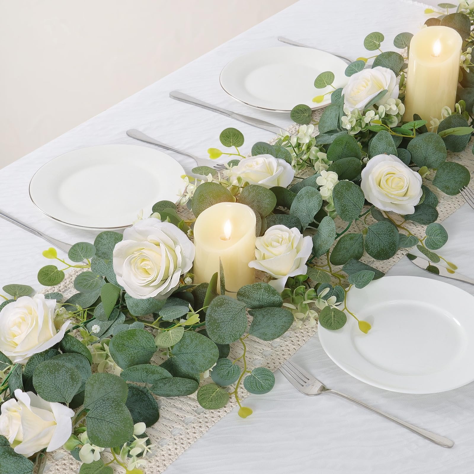 Artificial eucalyptus and white rose garland with candles on a table setting