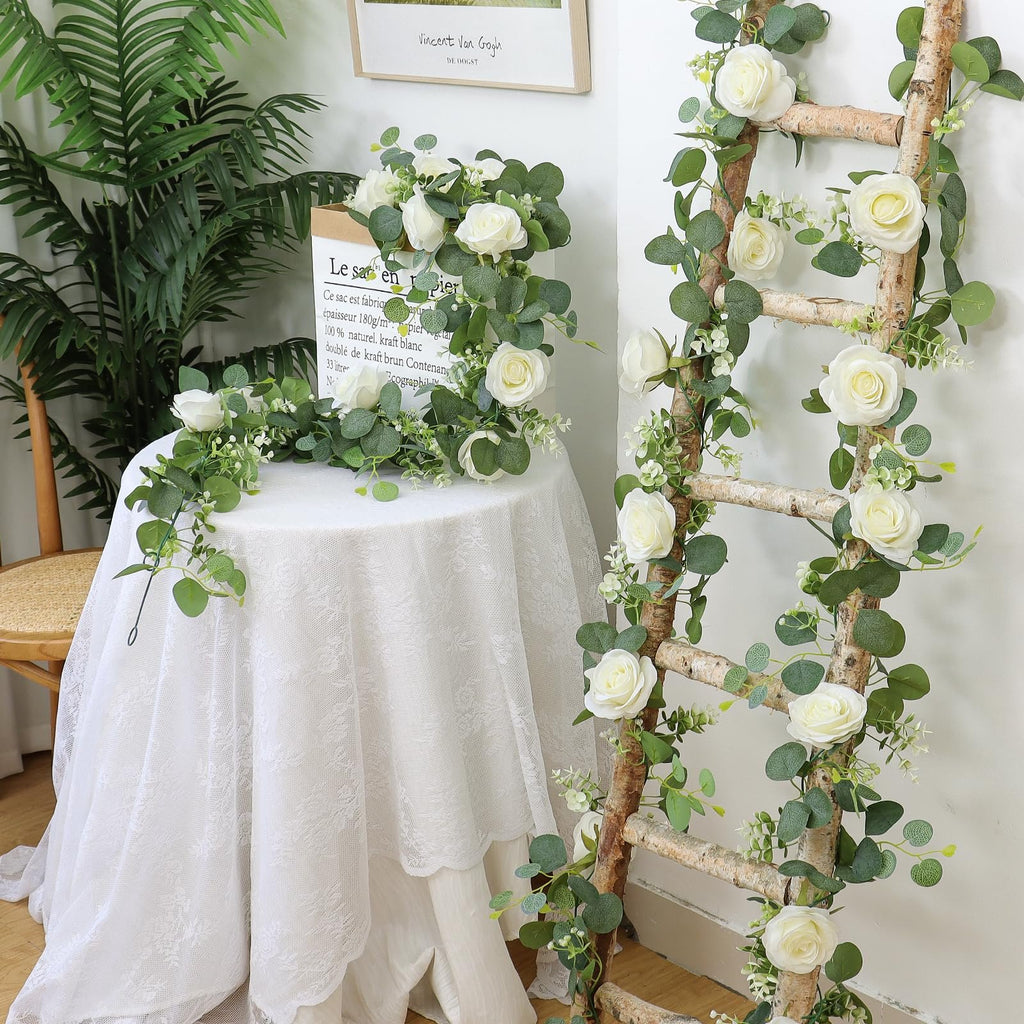 Artificial eucalyptus and white rose garland draped on a ladder and table