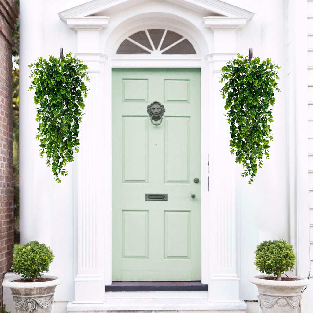 Two artificial hanging eucalyptus plants flanking a light green front door with a lion head knocker.