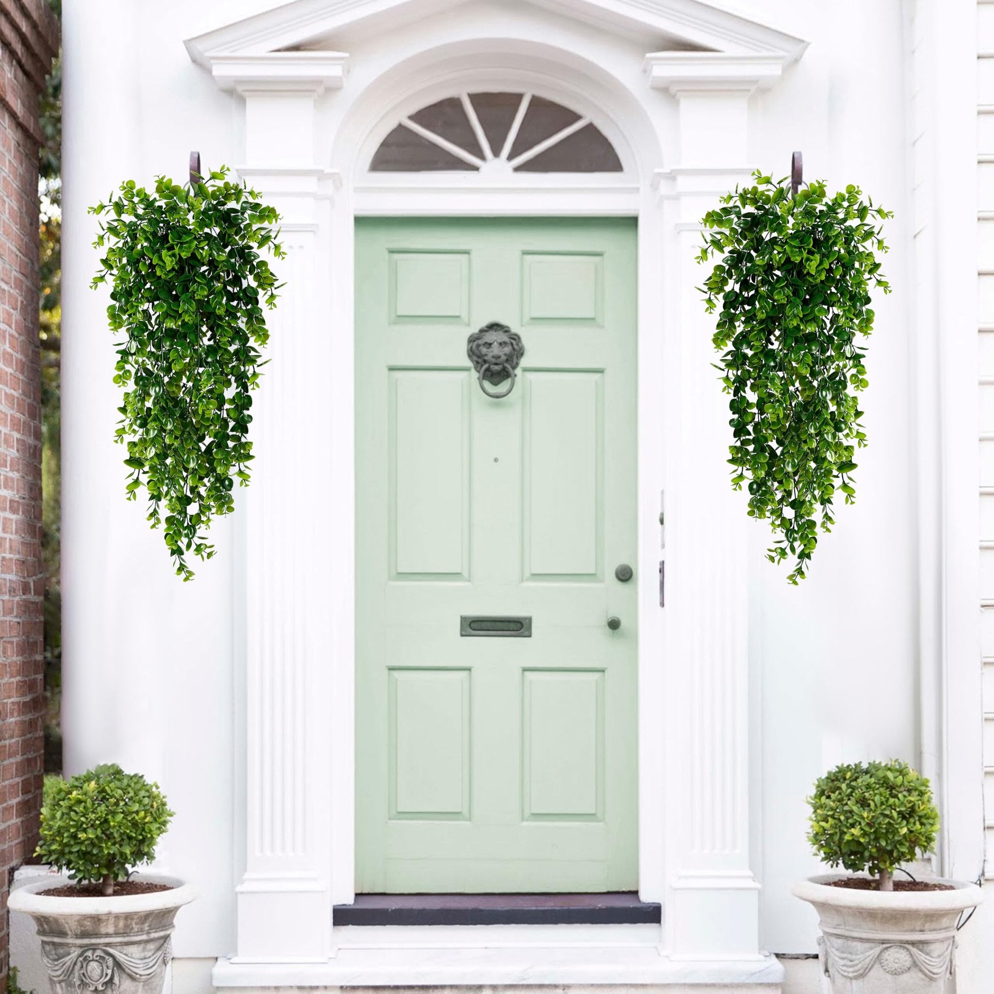 Two artificial hanging eucalyptus plants flanking a light green front door with a lion head knocker.