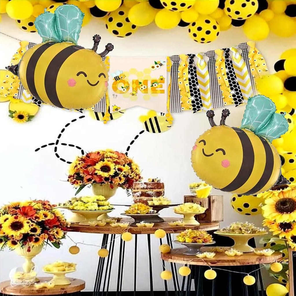 Bee-themed party decorations including balloons, a banner, and a dessert table with sunflowers.
