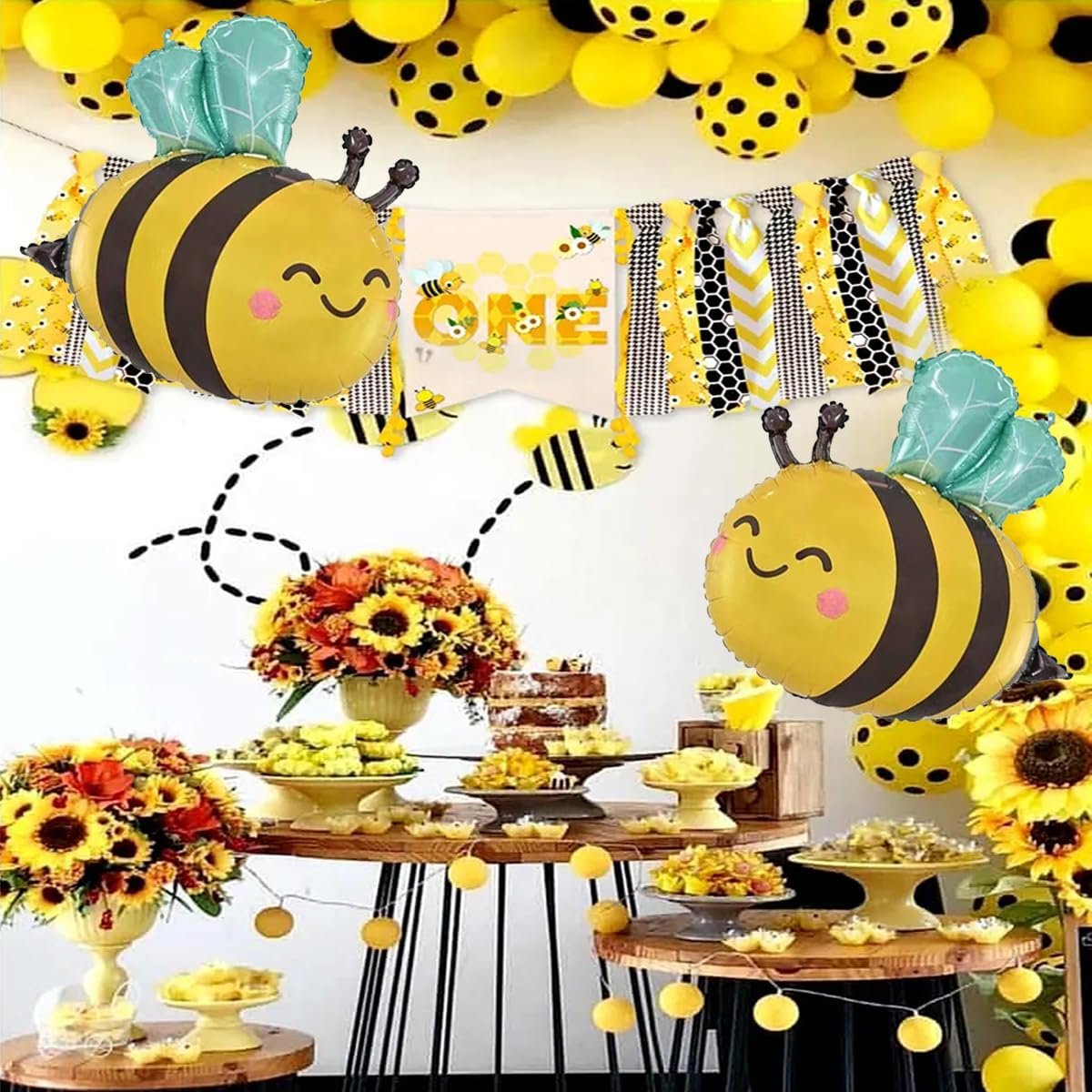 Bee-themed party decorations including balloons, a banner, and a dessert table with sunflowers.