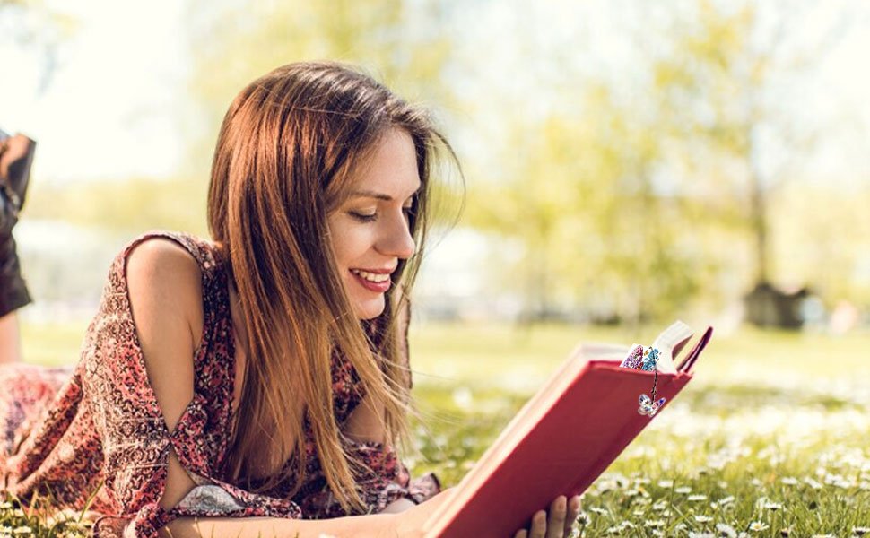 Woman reading a book in a grassy field with diamond art bookmarks attached
