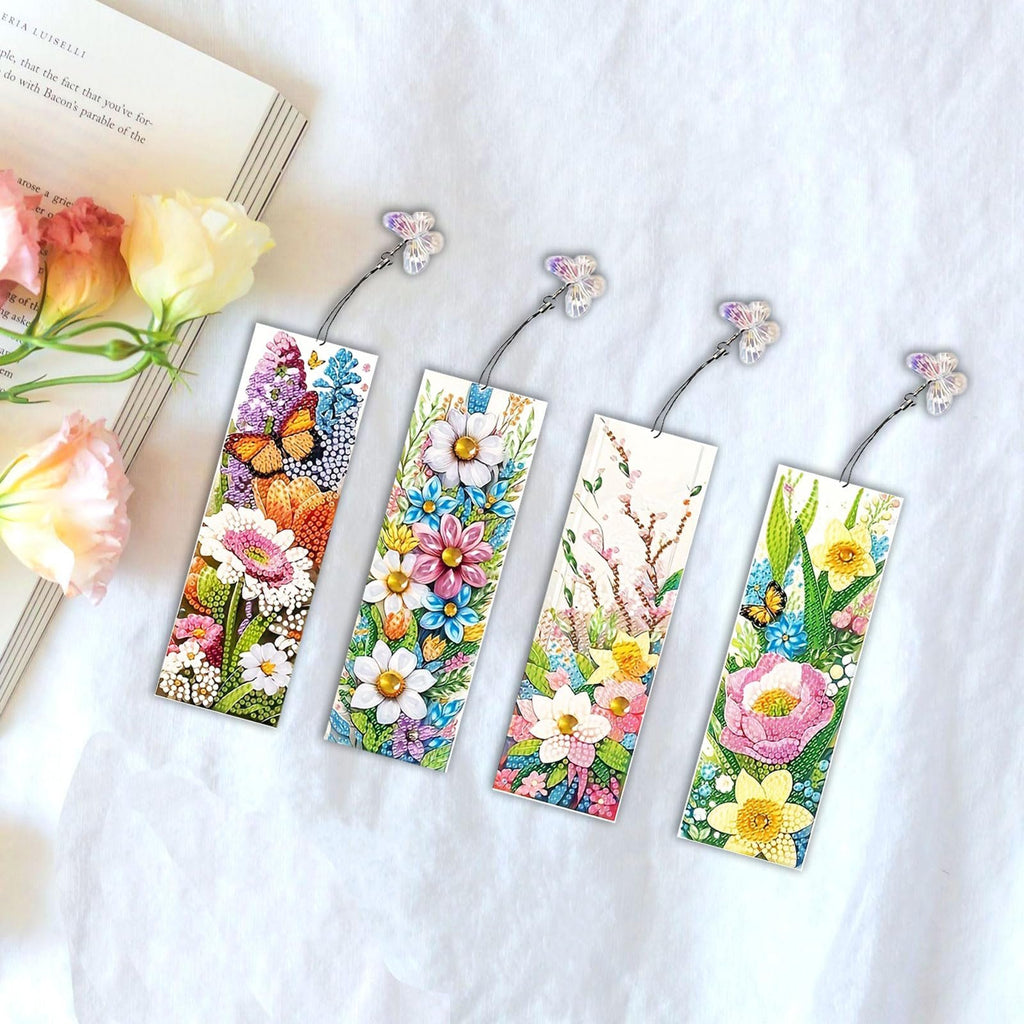 Four diamond art bookmarks with floral and butterfly designs, attached to a book with flowers.