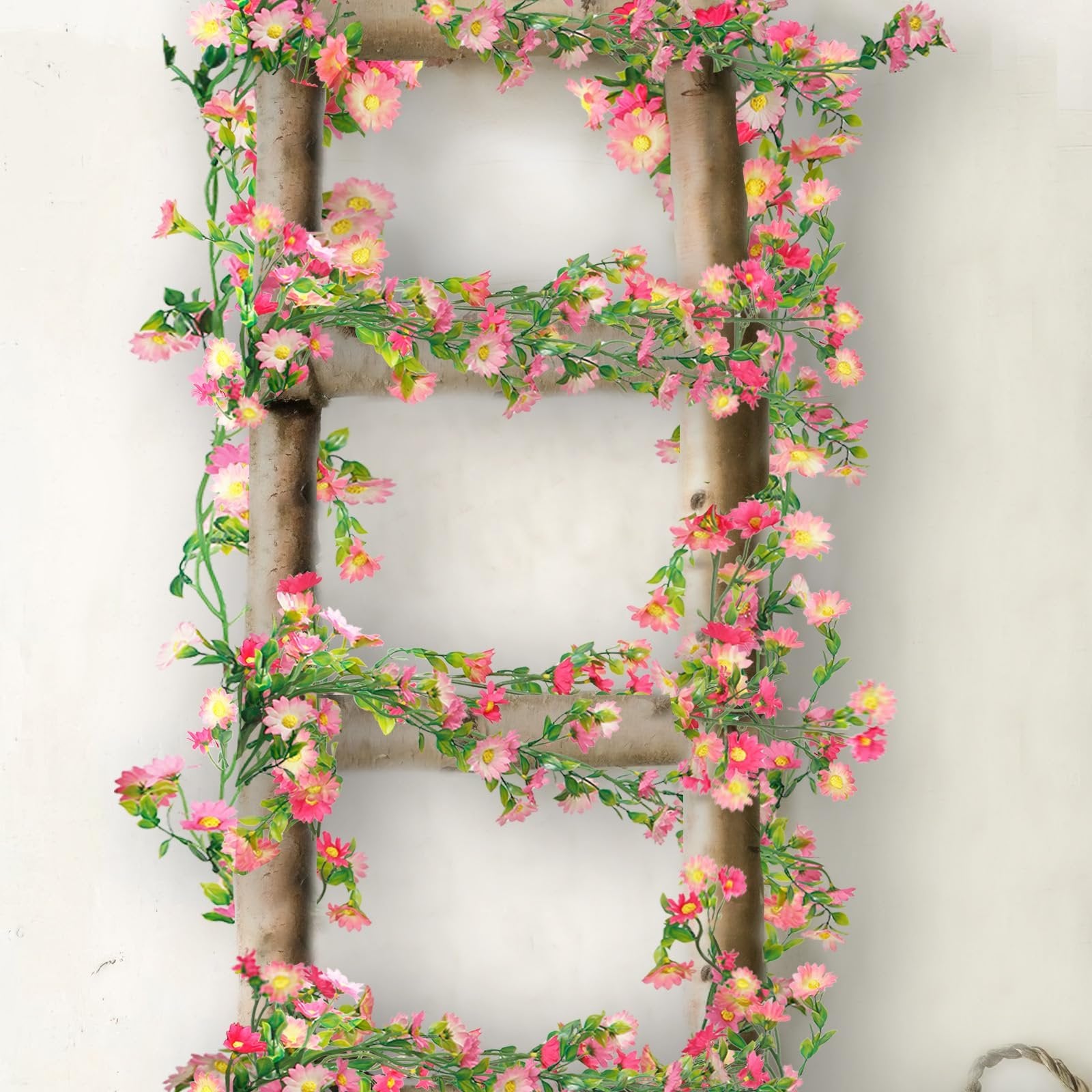 Artificial daisy flower garland with pink and rose red flowers and green leaves draped on a wooden ladder.