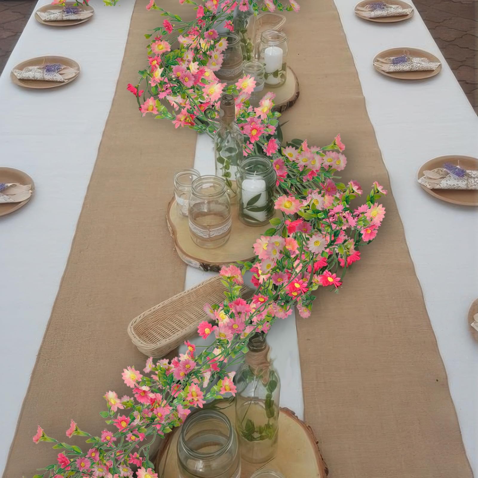 Artificial pink and rose red daisy flower garland with green leaves draped across a table setting with candles and plates.