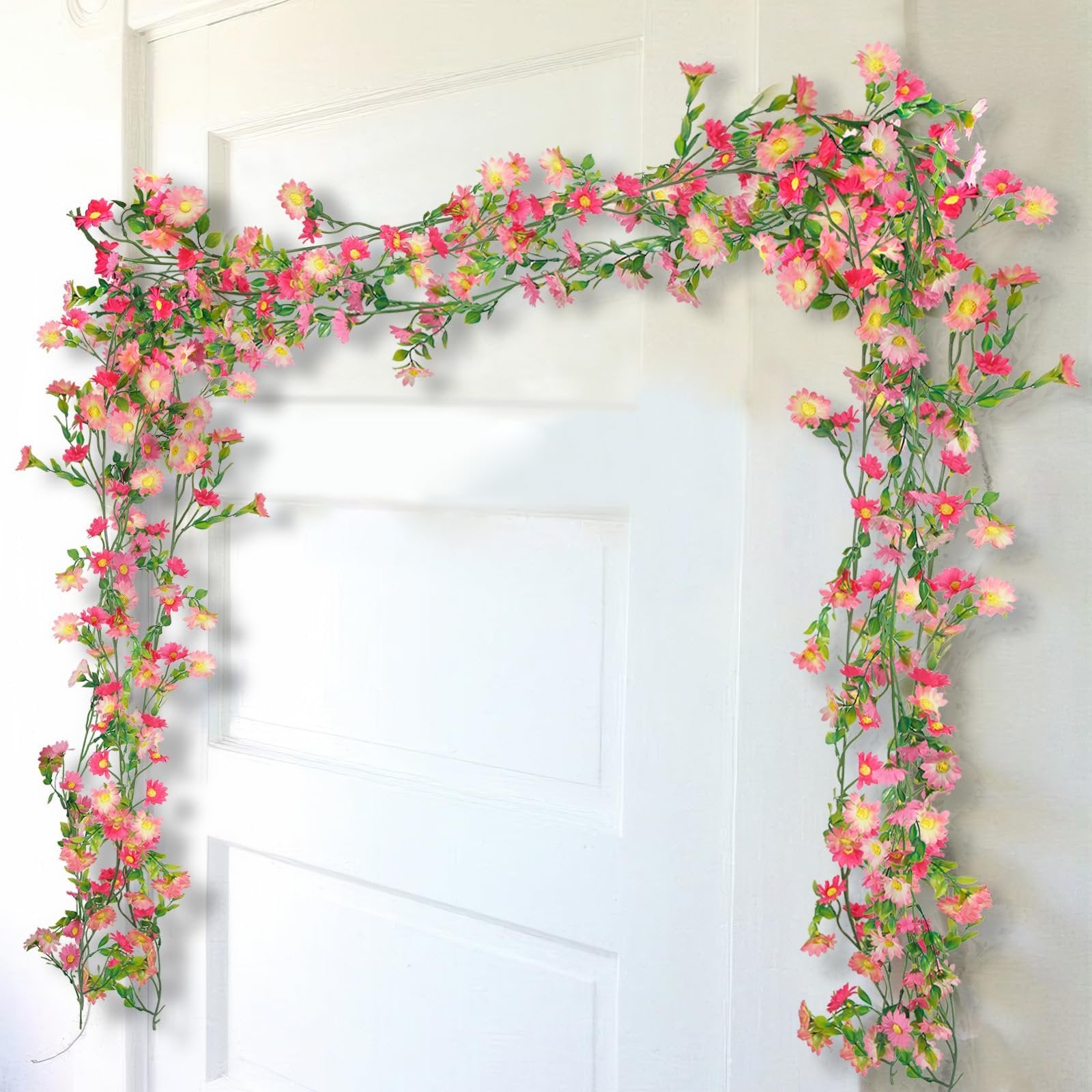 Artificial pink and rose red daisy flower garland with green leaves draped over a white door.