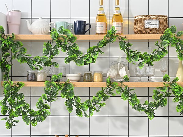 Artificial monstera leaf vines draped across kitchen shelves with decorative items.