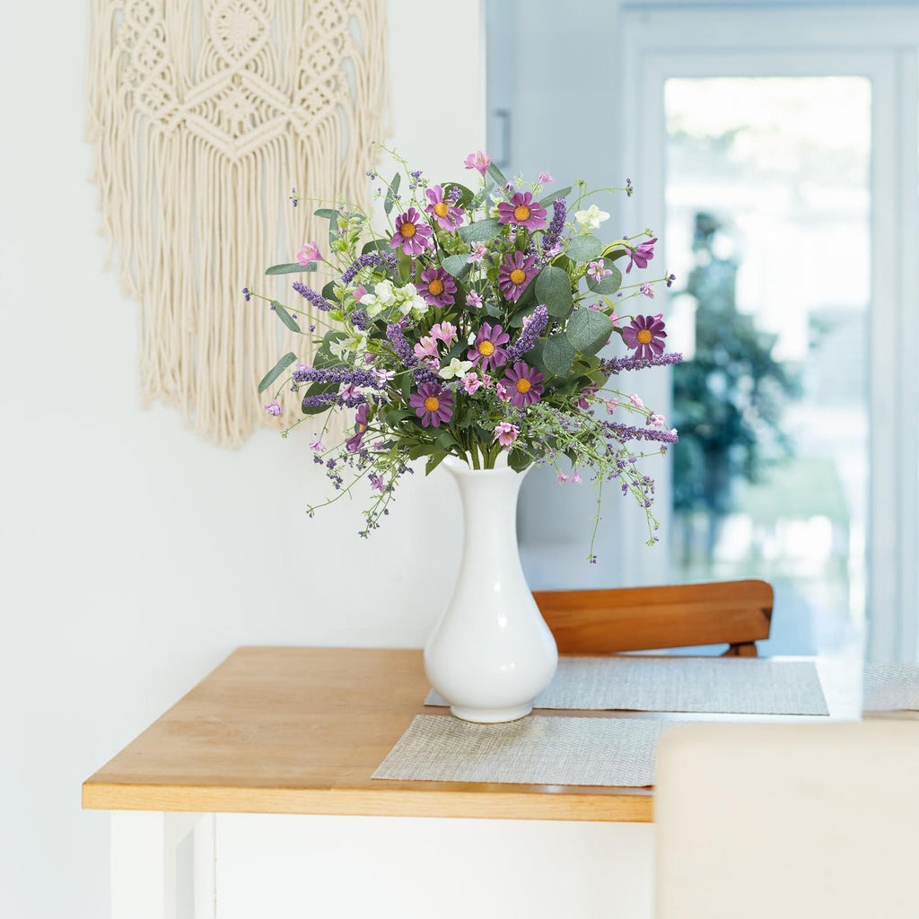 Artificial spring flower bouquet with purple daisies and lavender in a white vase on a wooden table