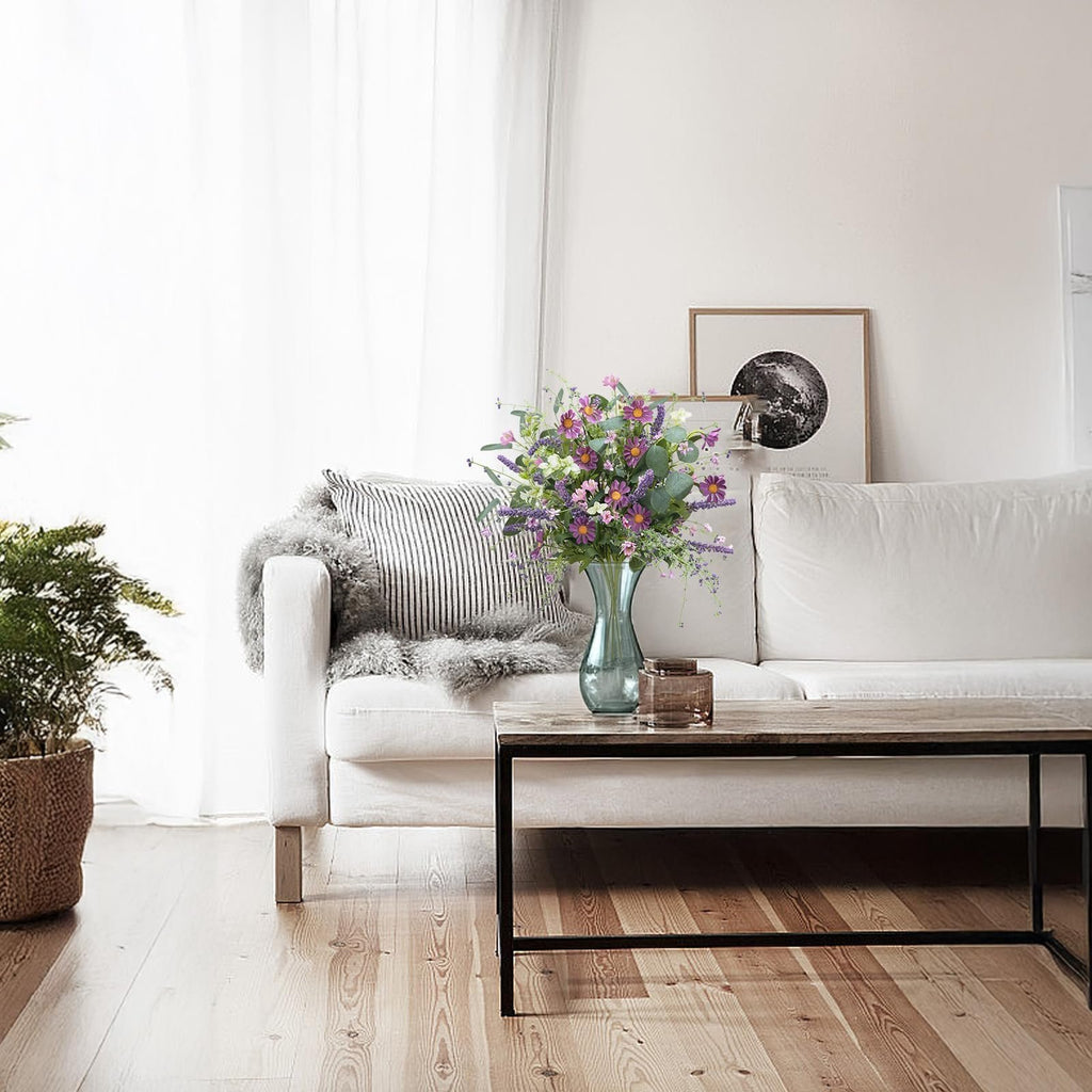 Artificial spring flower bouquet with purple daisies and eucalyptus leaves in a vase on a coffee table in a living room.
