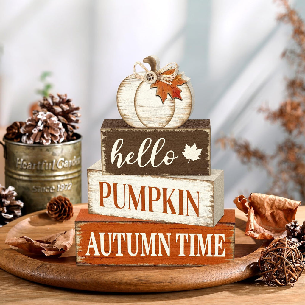 Stack of three wooden blocks with autumn-themed text and a decorative pumpkin on top, arranged on a wooden platter with pinecones.