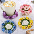 Four crocheted flower coasters with a mug of coffee on one, on a white textured surface.