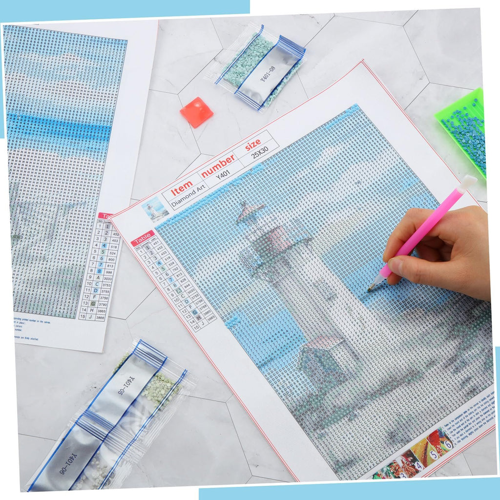 Diamond art painting kit with lighthouse design, showing a hand using a pink tool to place beads on a numbered canvas, with bags of beads and a color chart.