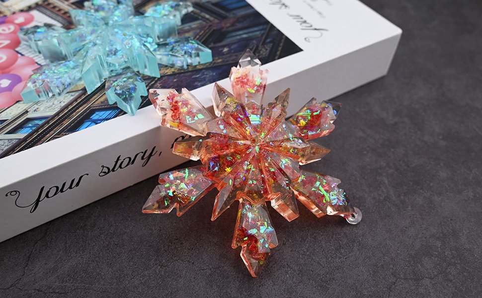 Two large snowflake resin ornaments, one orange and one blue, displayed on a book with text.