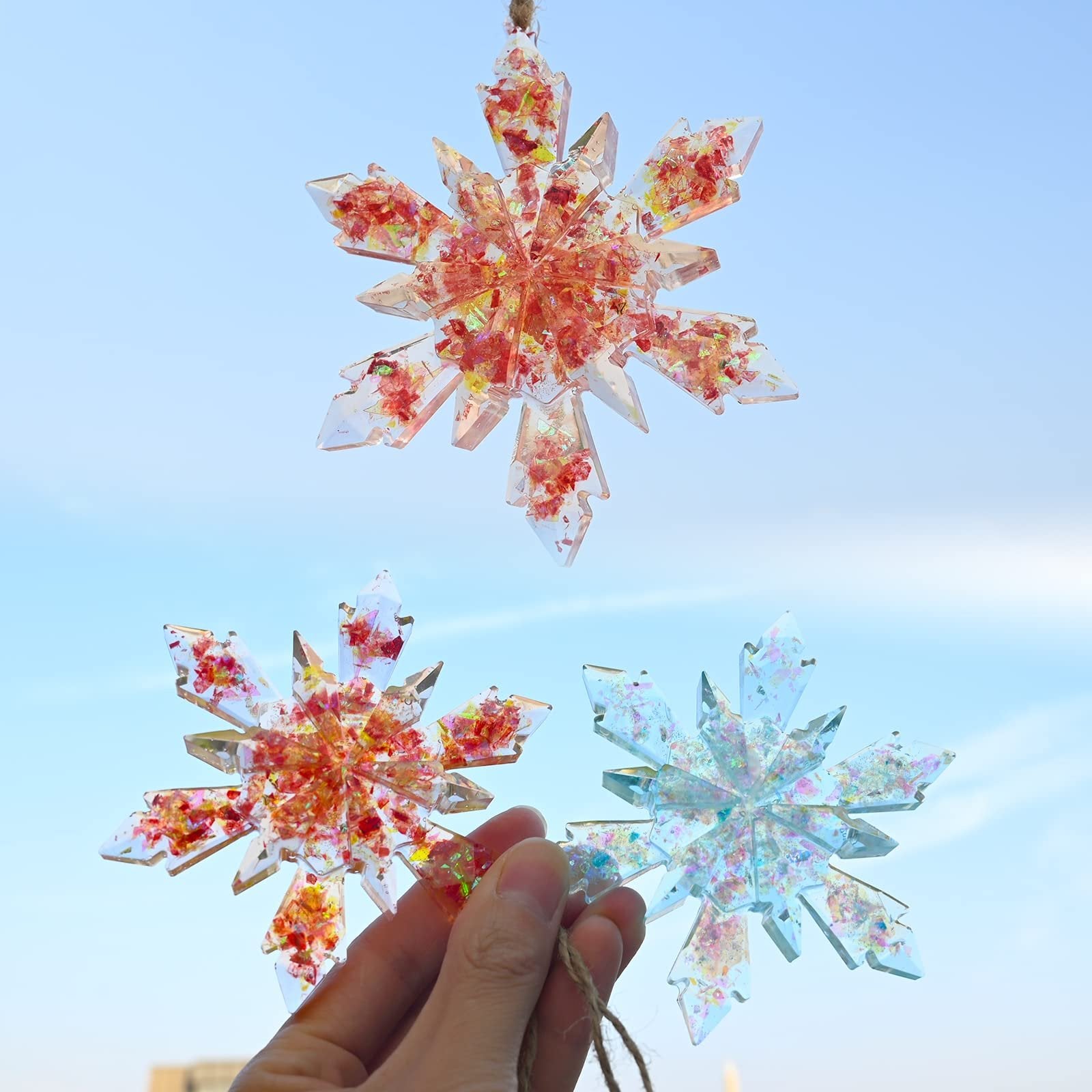Three clear snowflake ornaments with red and blue glitter suspended inside, held against a blue sky.