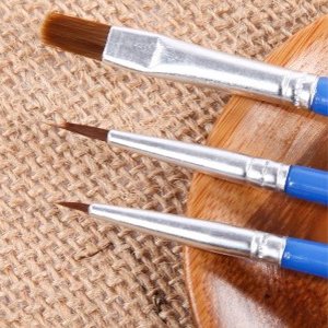 Three paint brushes with blue handles and silver ferrules on a burlap and wood surface