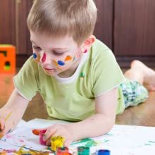 Young boy with paint on his face and shirt lying on the floor and painting