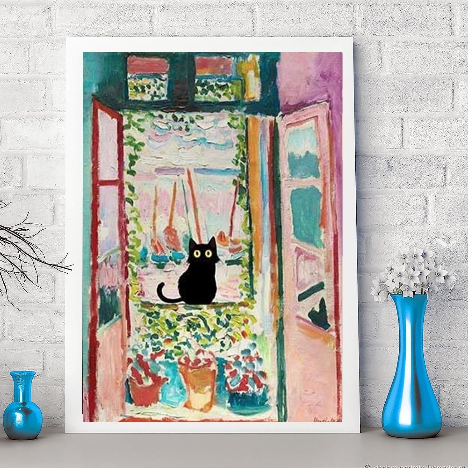 Black cat sitting on a windowsill with potted plants, framed artwork on a brick wall.