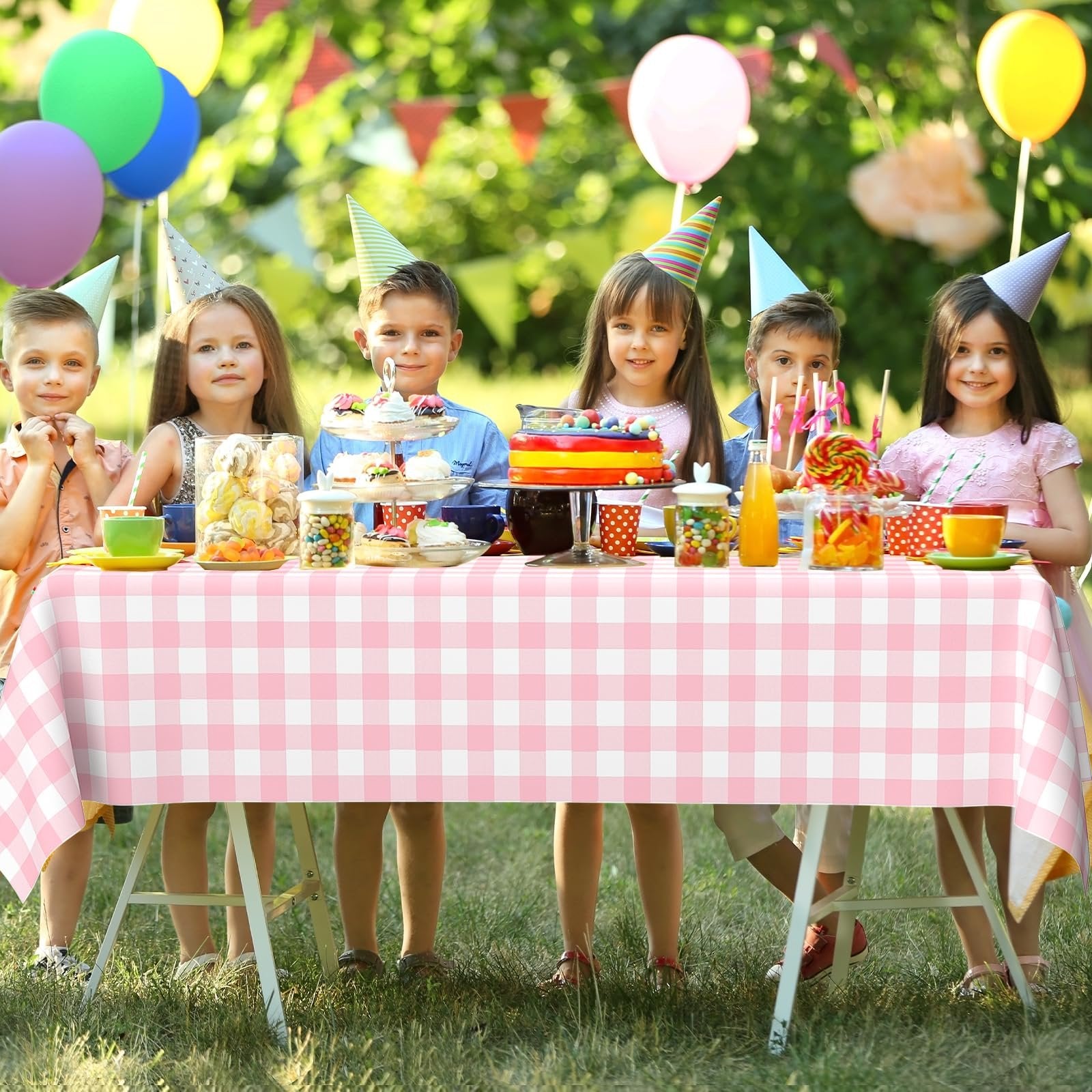 Children at a party table covered with a pink gingham disposable tablecloth, with cake, candy, and balloons.