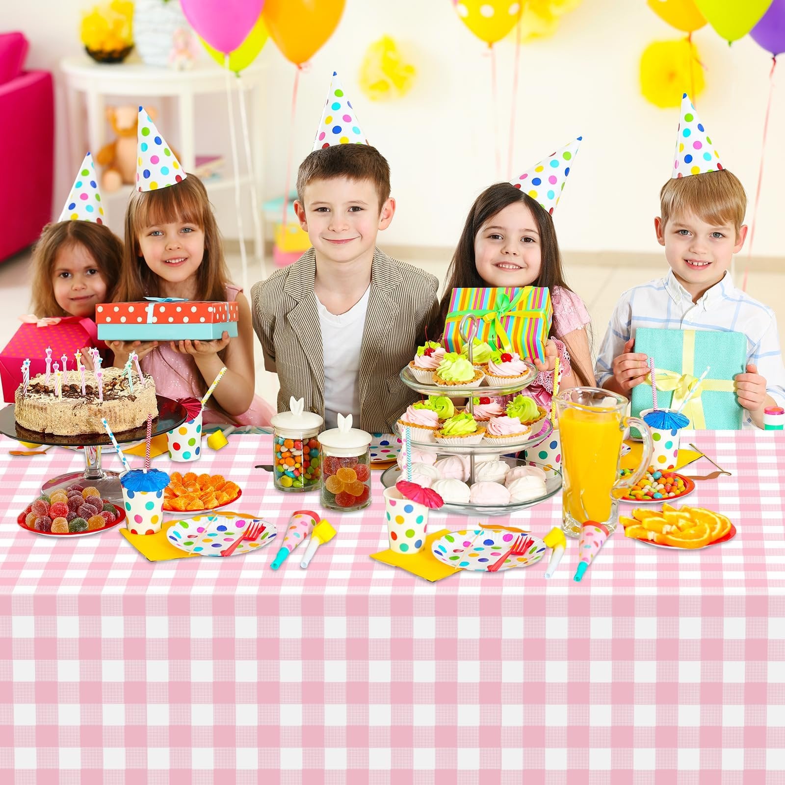 Five children wearing party hats sit behind a table laden with birthday treats, including a cake, cupcakes, candy, and drinks.