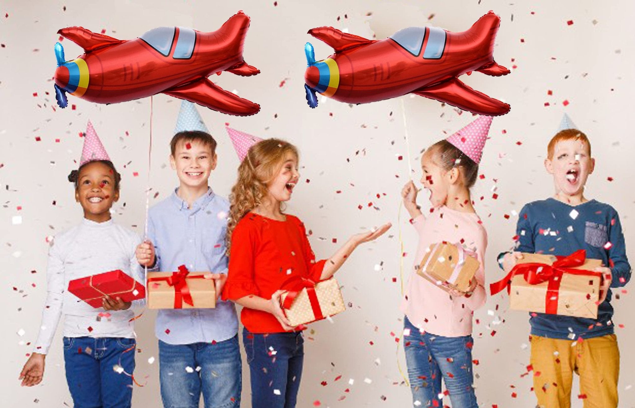 Five children in party hats holding gifts with red airplane balloons overhead and confetti falling