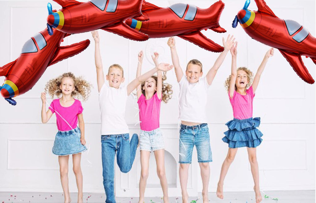 Five children jumping with red airplane foil balloons overhead at a party