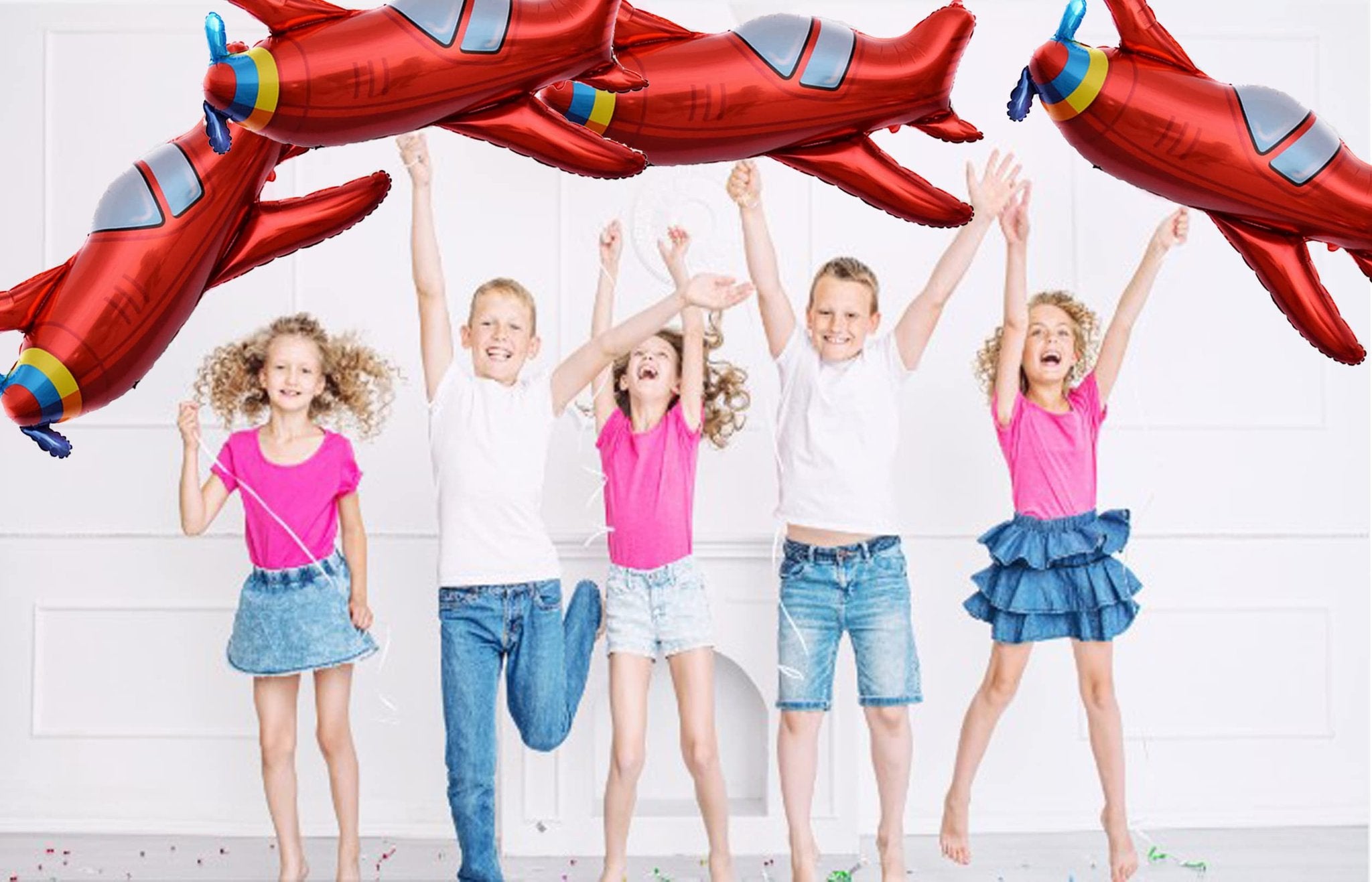 Five children jumping with red airplane foil balloons overhead at a party
