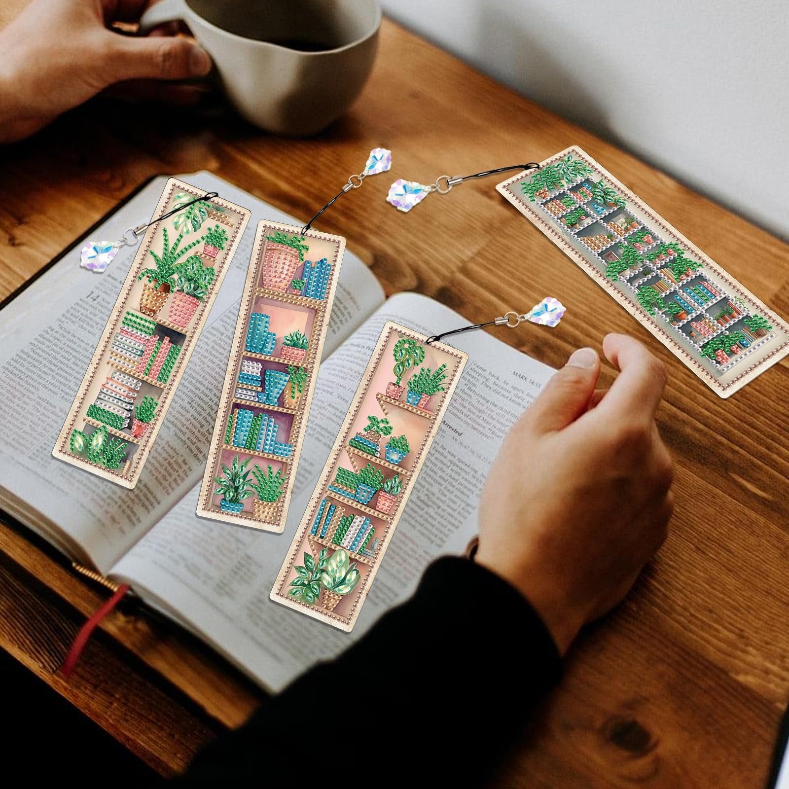 Four diamond painting bookmarks with plant and bookshelf designs resting on an open book.