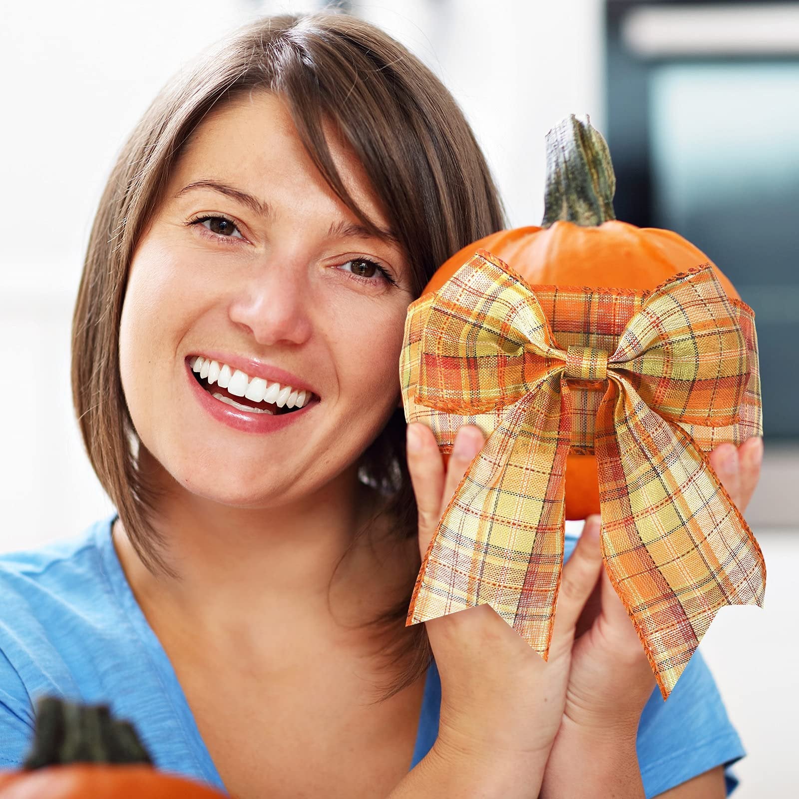 Woman smiling and holding a pumpkin decorated with a plaid bow