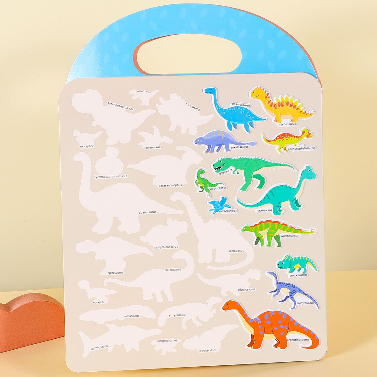 Dinosaur sticker book with various dinosaur shapes and corresponding names on a light background. Colorful dinosaur stickers are placed on the page.