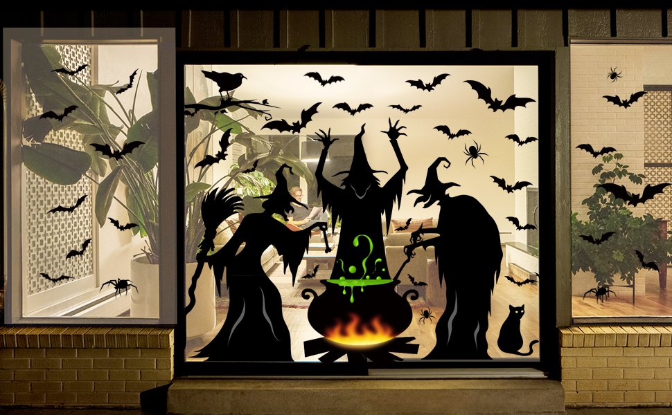 Halloween window clings featuring witches, bats, spiders, and a cauldron silhouette applied to a storefront window at night.