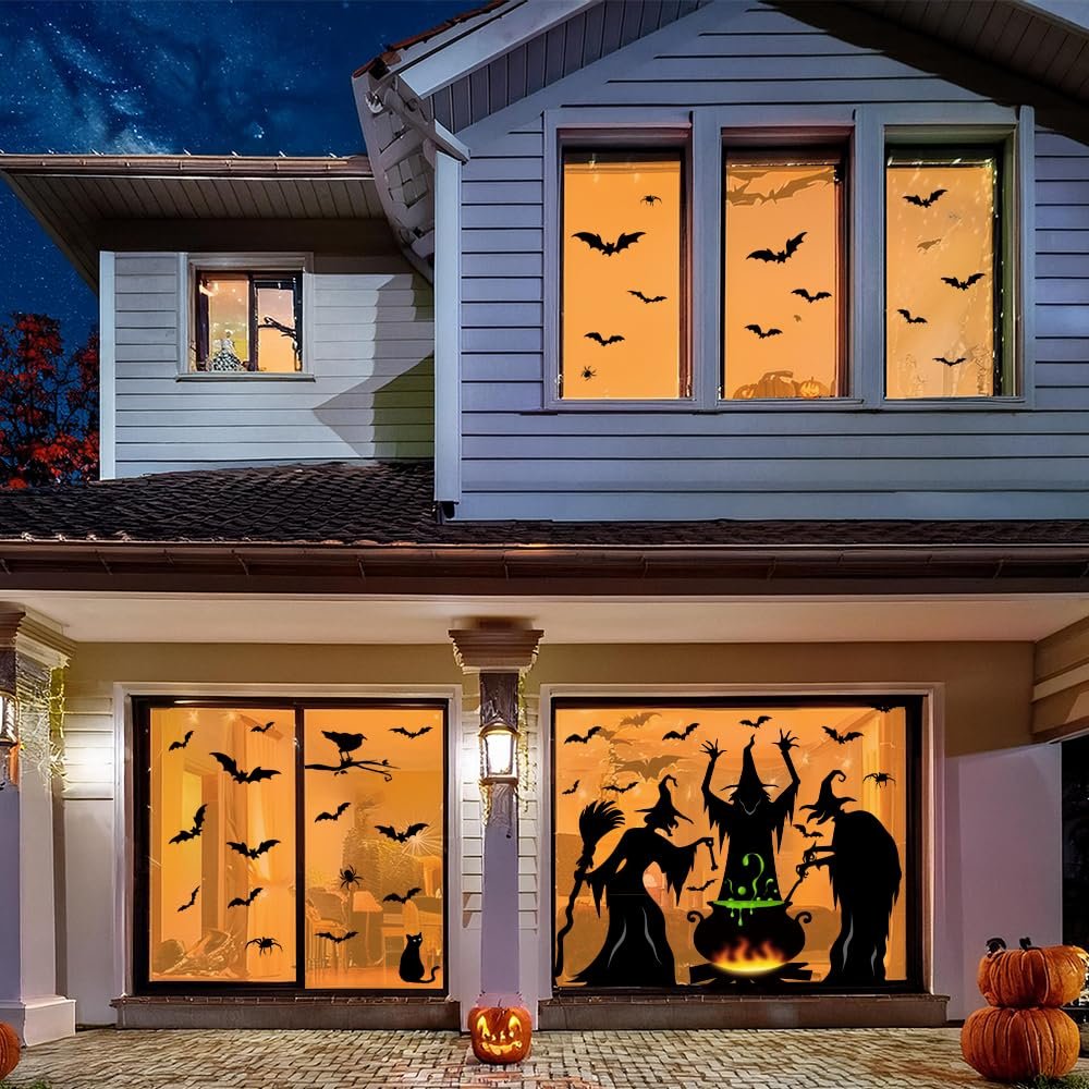House decorated with Halloween window clings featuring bats, spiders, witches, and a cauldron silhouette at night.