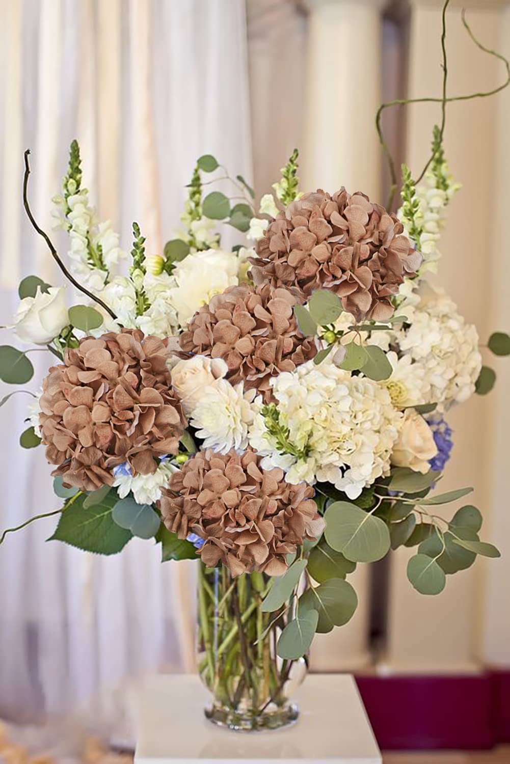 Arrangement of artificial orange hydrangeas and white flowers in a glass vase, front view.