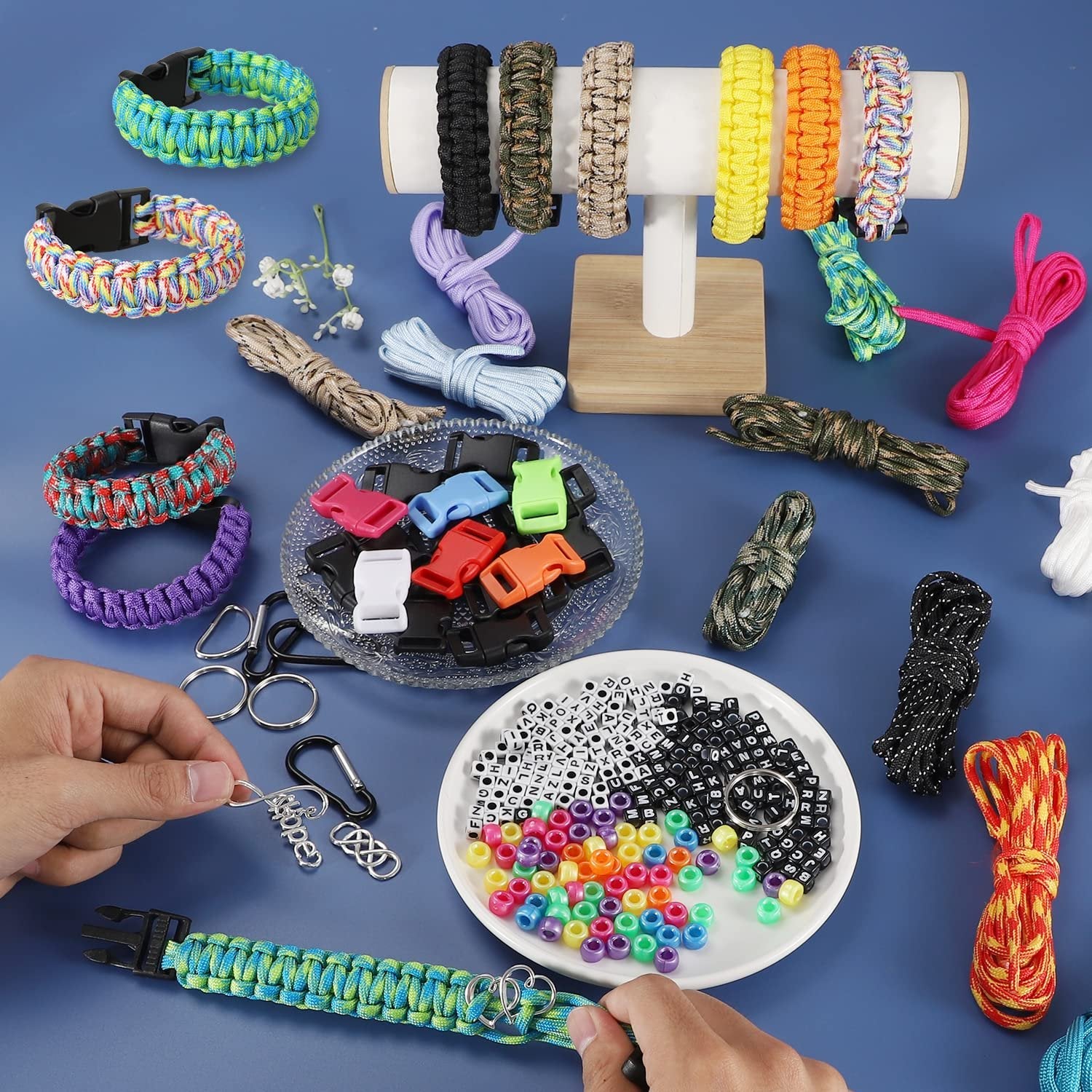 Paracord bracelet making kit with various colored cords, buckles, beads, and tools laid out on a blue surface.
