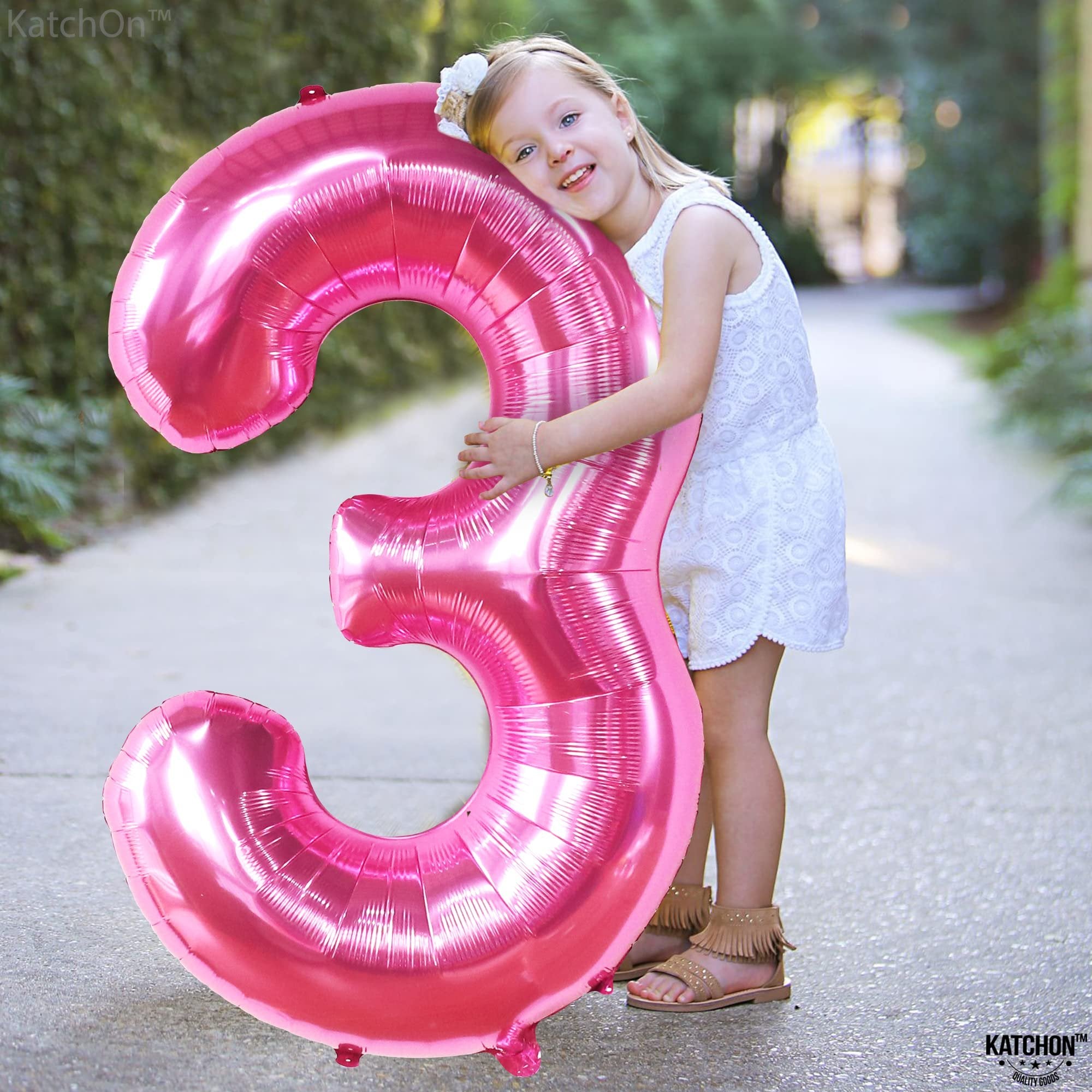 Young girl hugging a large hot pink number 3 foil balloon outdoors