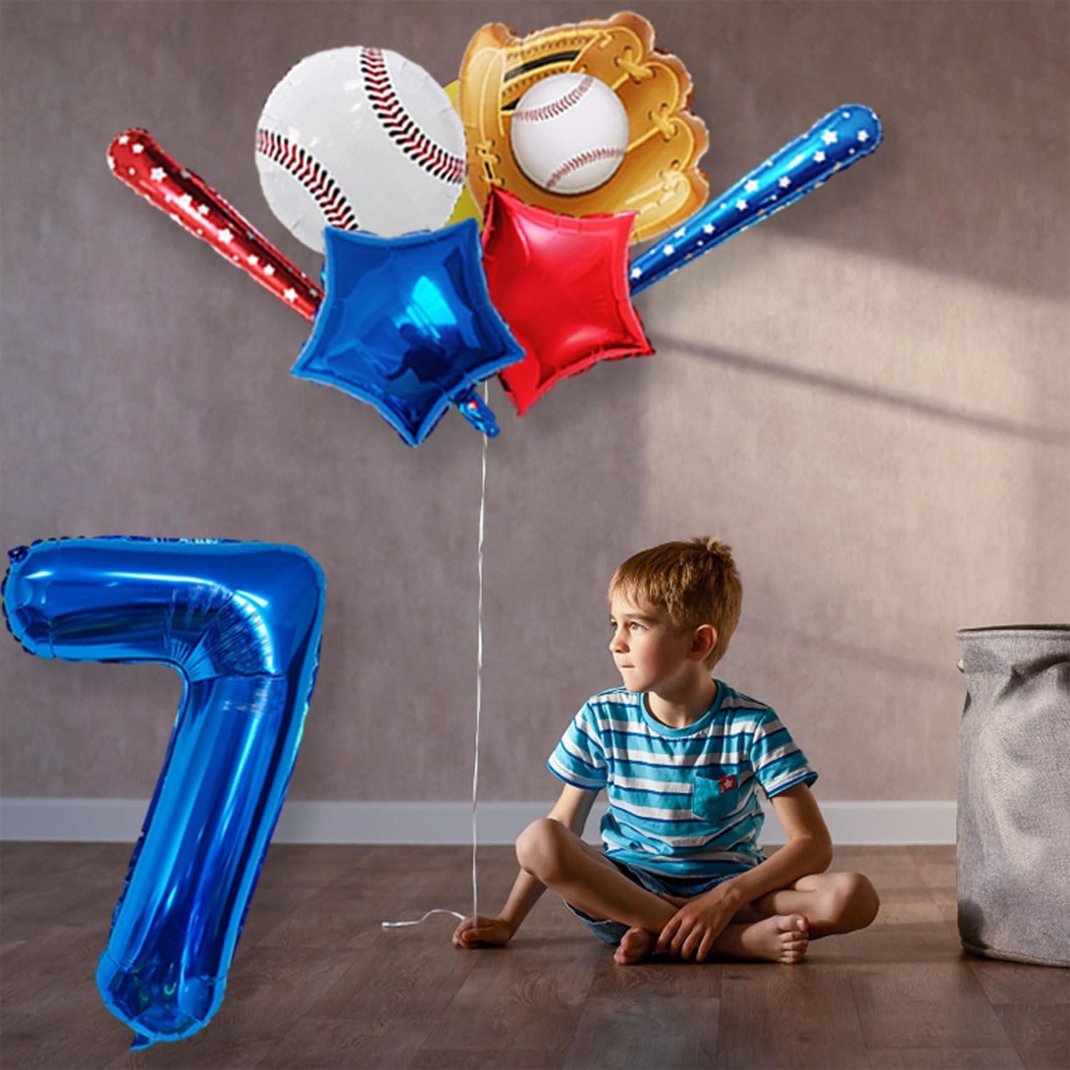 Boy sitting on floor with a large blue number 7 balloon and baseball-themed balloons