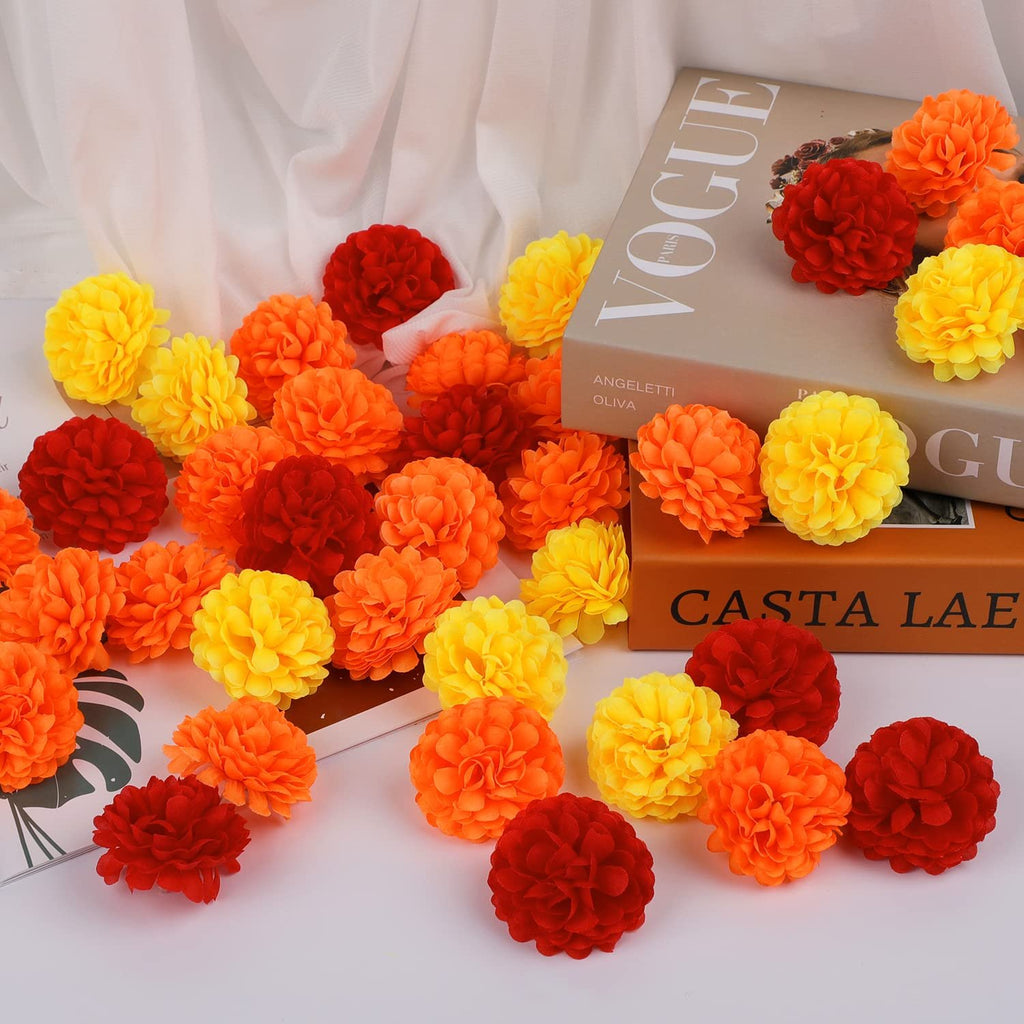 Artificial marigold flower heads in red, orange, and yellow scattered around books.