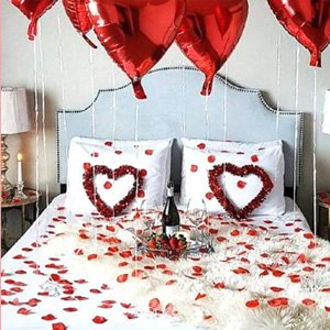 Valentine's Day bedroom decor with heart balloons, rose petals, and wine glasses on a bed.
