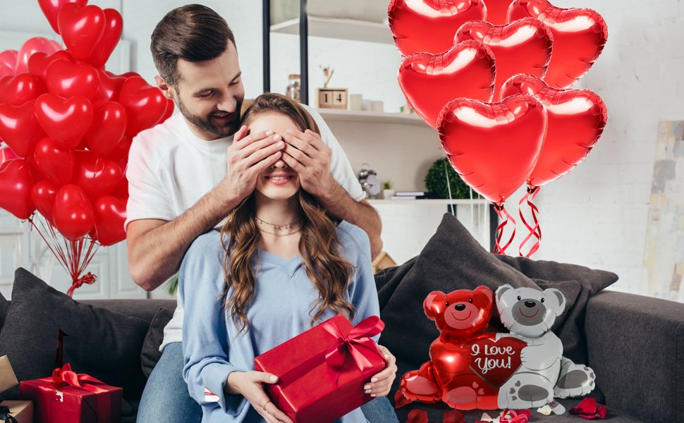 Couple celebrating Valentine's Day with heart balloons and teddy bear balloons, woman receiving a gift