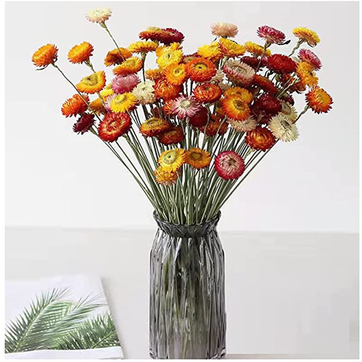 Vase filled with a colorful bouquet of dried daisies in shades of orange, yellow, red, and pink.
