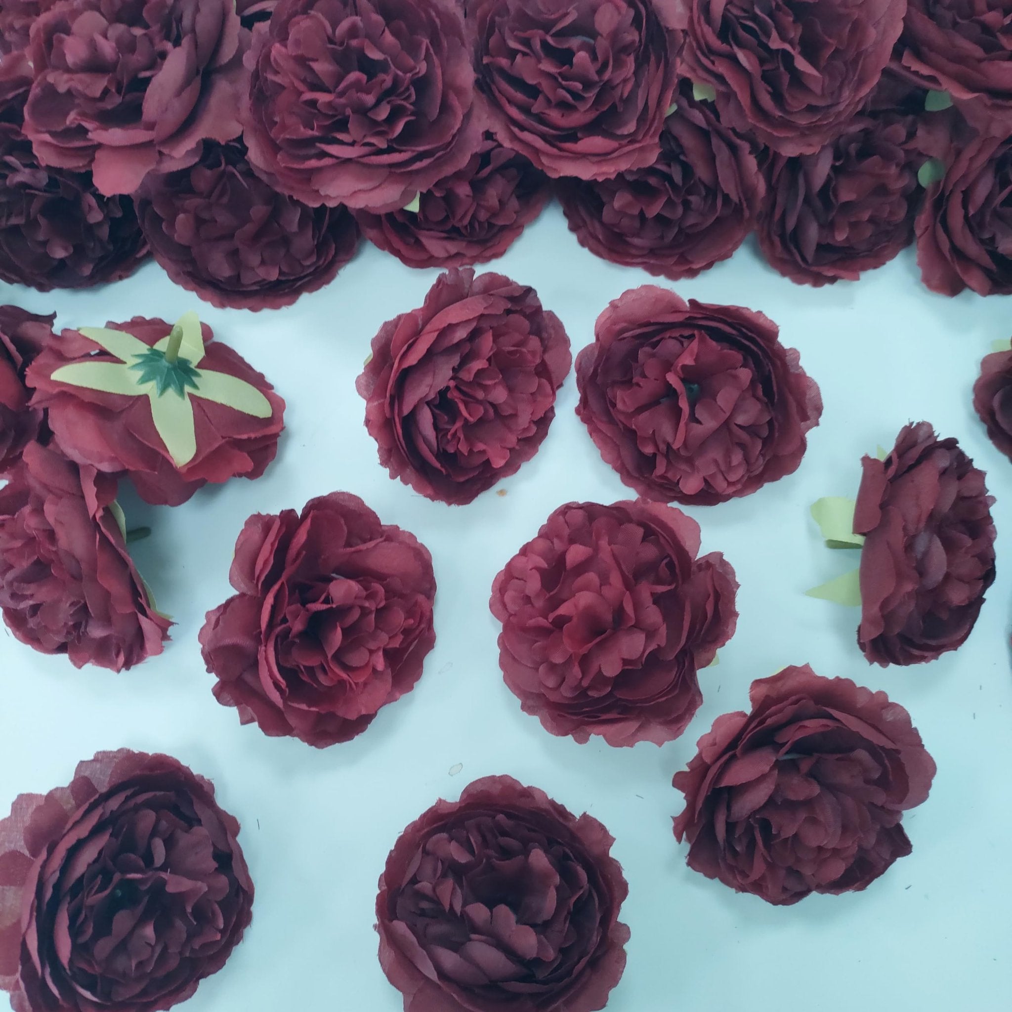 Burgundy artificial rose heads scattered on a white surface, some showing green calyx and stem base.