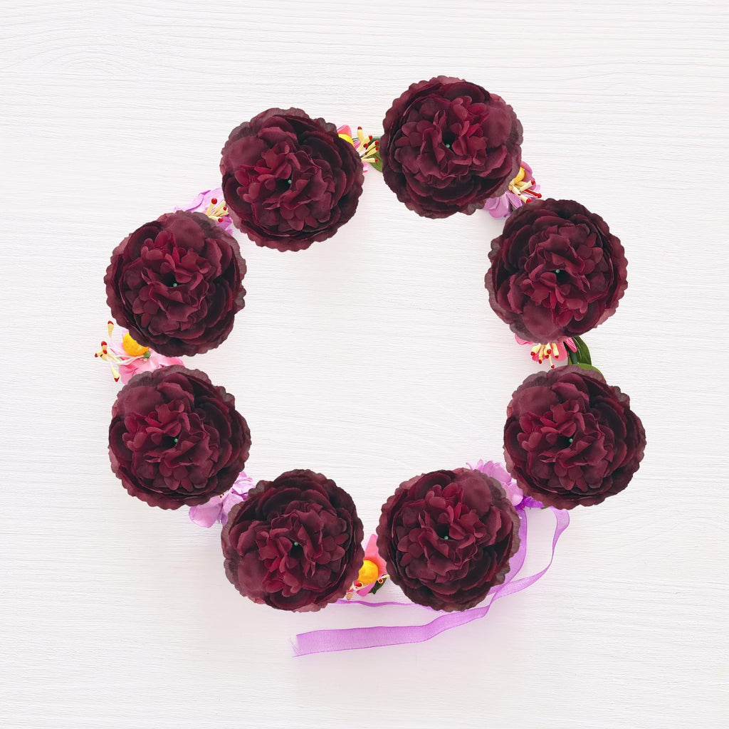 Burgundy silk rose heads arranged in a circular wreath on a white wooden background with purple ribbon accents