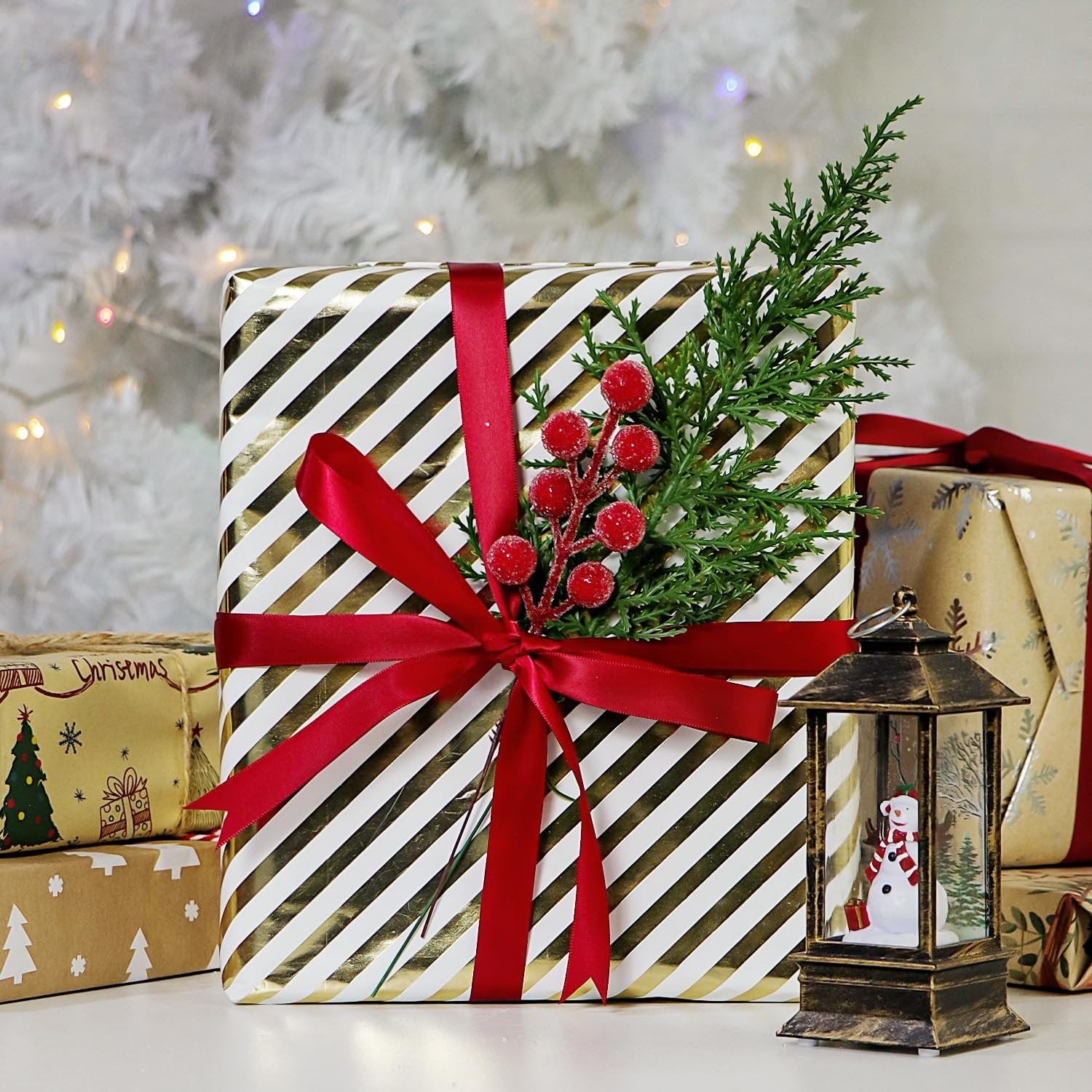 Wrapped Christmas gifts with red ribbon and artificial pine branches with red berries, next to a lantern with a snowman inside.